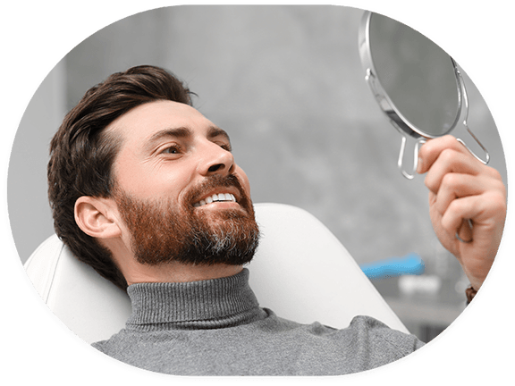 Bearded man in dental chair checking smile in handheld mirror