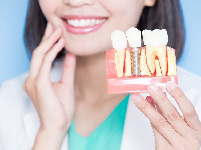 Dentist holding model dental implant and touching her jaw in the background