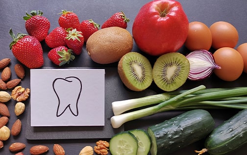 A drawing of a tooth on a counter surrounded by fruits, veggies, nuts, and eggs