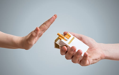 A hand refusing the offering of a cigarette with a pale background