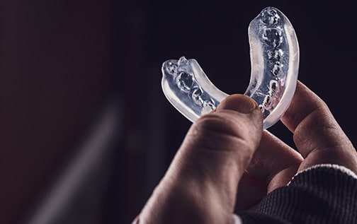 Two fingers holding a clear mouthguard with a dark background